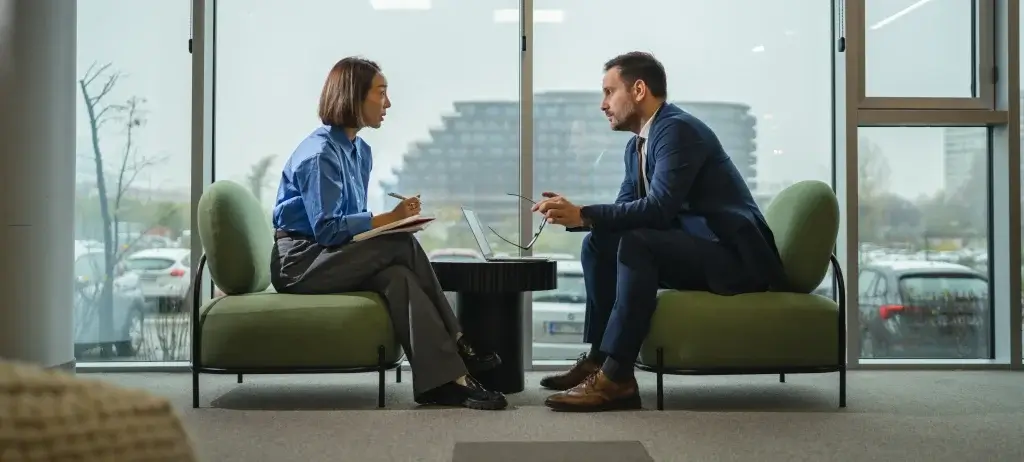 An employment solicitor in a blue shirt reviewing a contract on a laptop while advising a male client in a suit about settlement agreements, redundancy procedures, and workplace legal disputes.